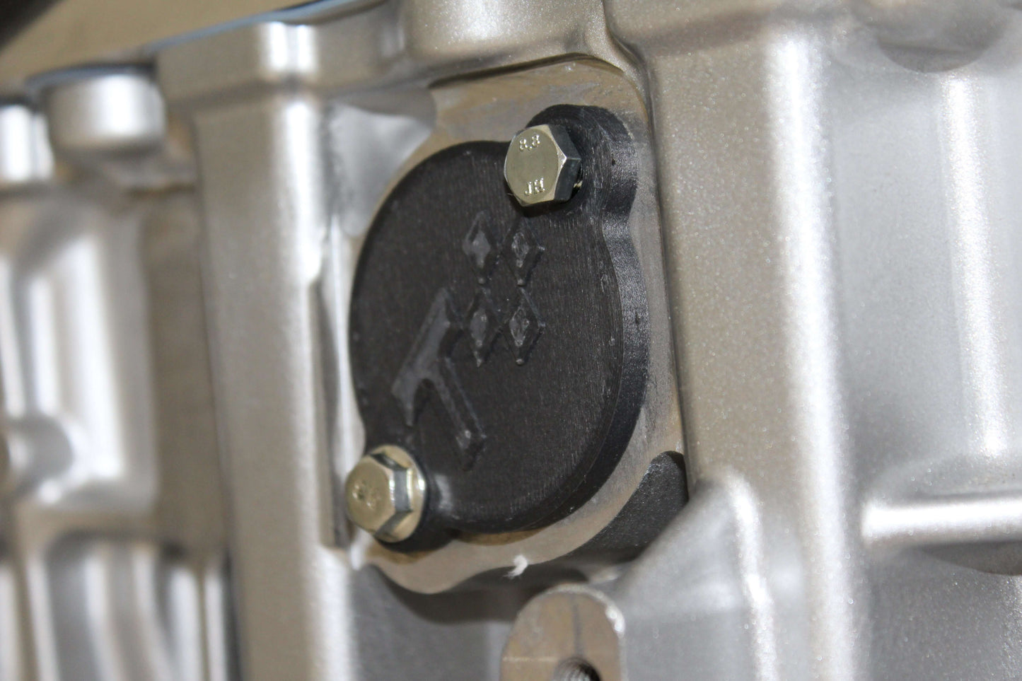 Close-up of N52 engine with black injector port cover secured by bolts, showcasing durable craftsmanship.