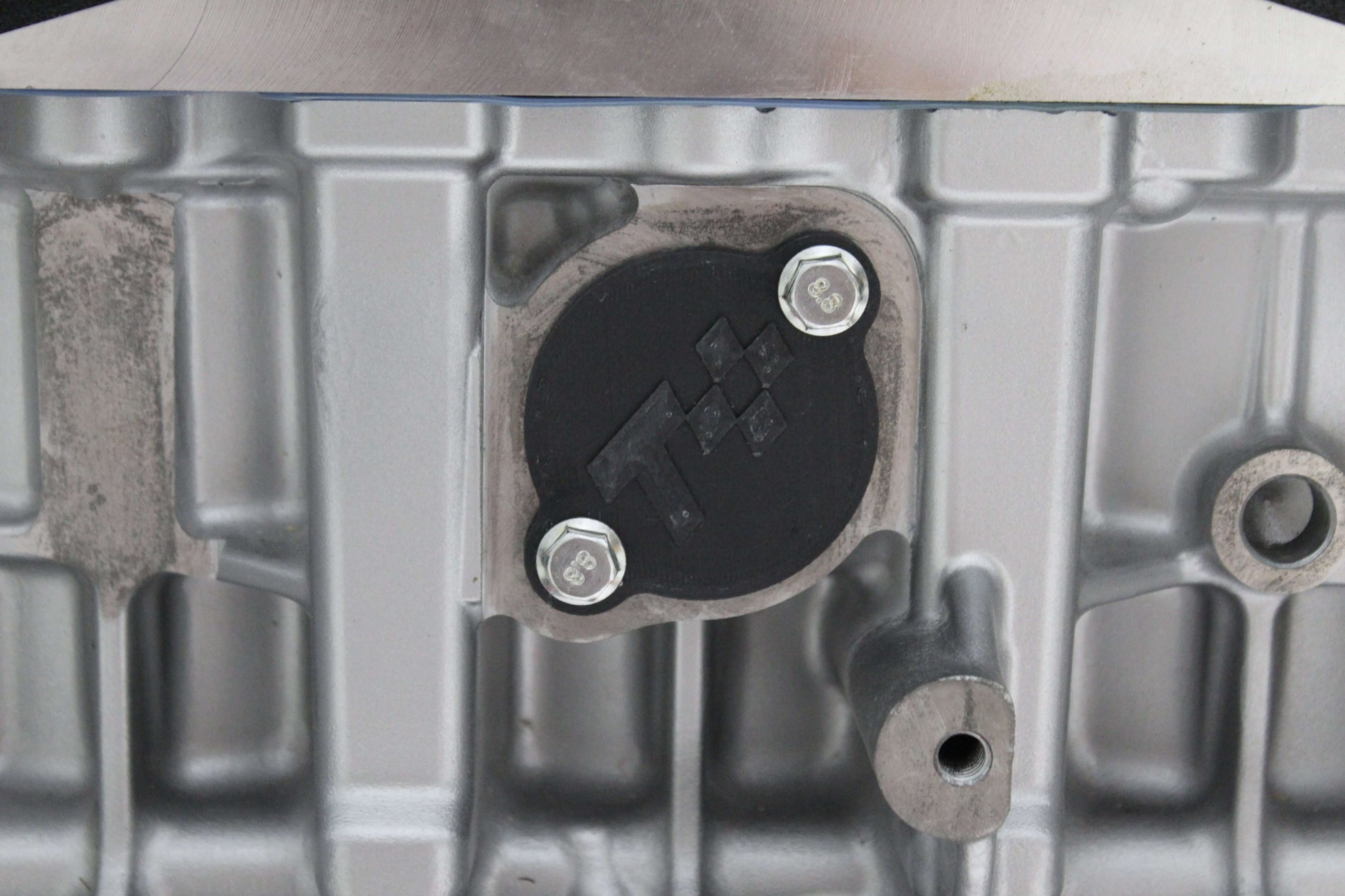 Close-up of N52 injector port cover showing bolts and engine block for maintenance and repair.