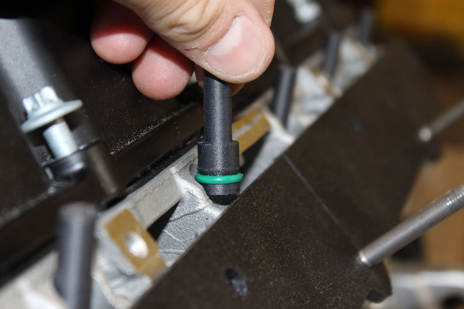 Close-up of hand installing an N52 injector port cover in an engine, showcasing detailed engine maintenance.